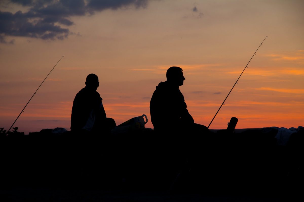 Pfingsten: zwei angler sitzen am Wasser während die Sonne untergeht.