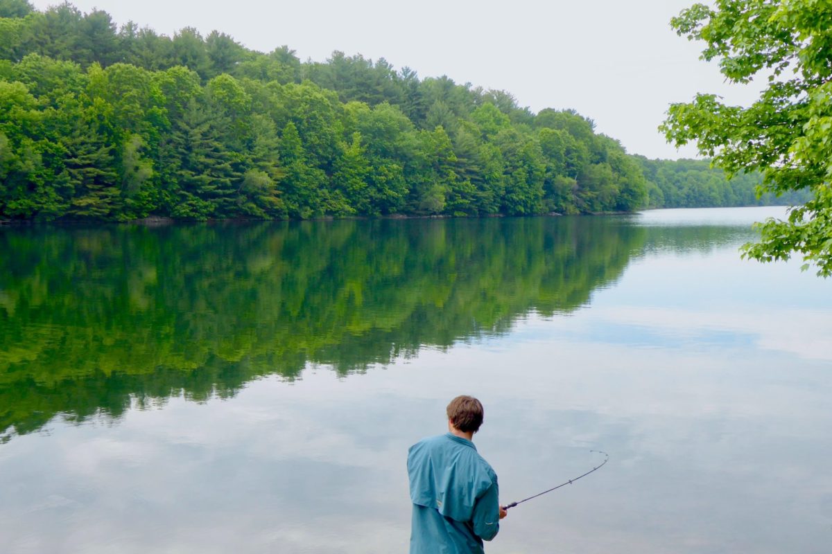 Ein Angler steht am Rande eines Sees im Wald und angelt.