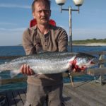 EIn Angler steht mit einer großen Meerforelle in der Hand auf der Seebrücke in Wustrow.