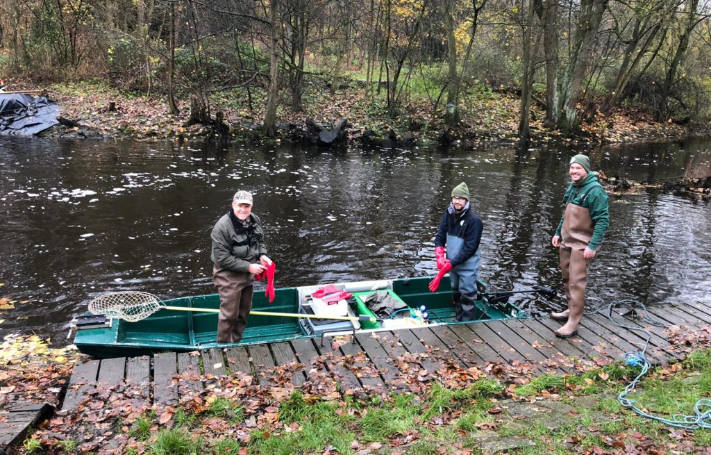 Drei Angler betreten ein Boot am Flussrand.