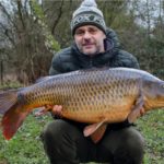 Angler hält gefangenen Karpfen in die Kamera.