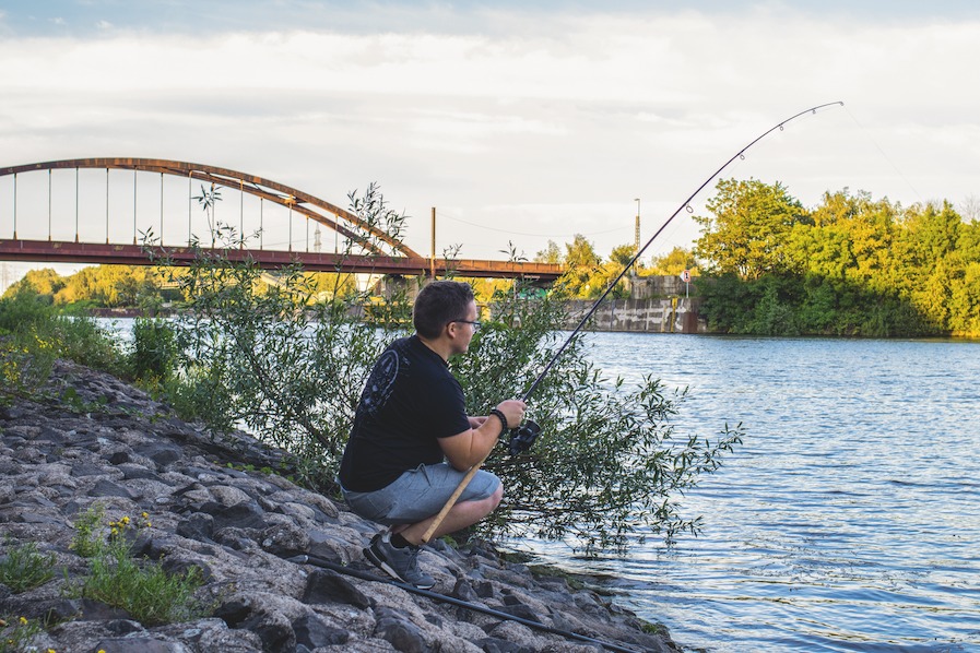 Angler sitzt an Wasserkante mit ausgeworfener Angel.