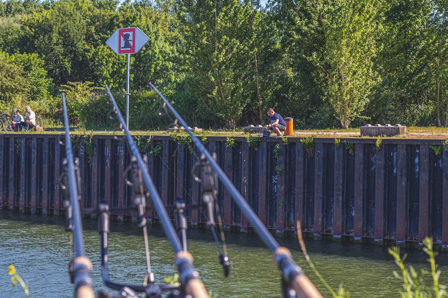 Angler sitzen an Spundwand mit mehreren Angeln im Gestell.