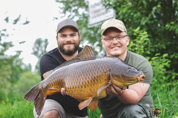 Zwei Angler halten gefangenen Karpfen vor.