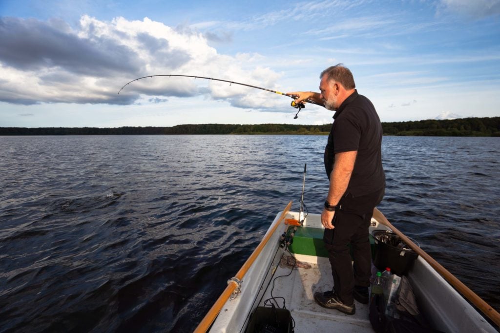 Angler auf Ruderboot drillt einen Hecht im frühen Herbst