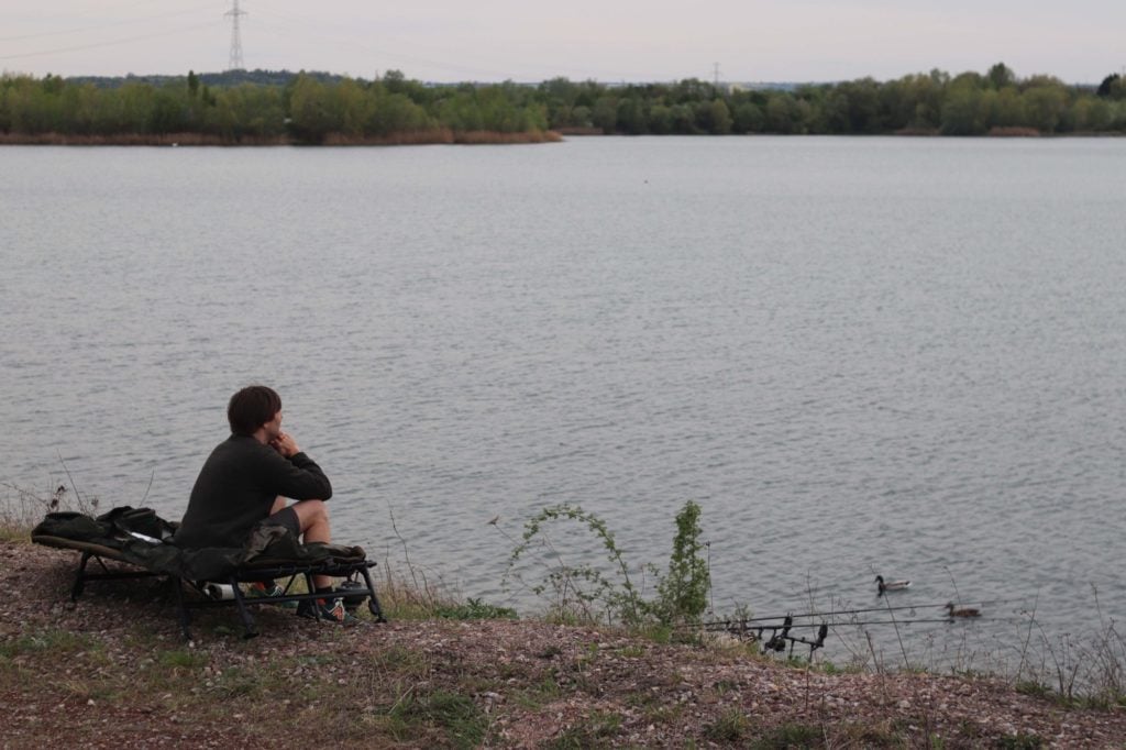 Karpfenangler auf seiner Liege, ohne Zelt, blickt auf den See