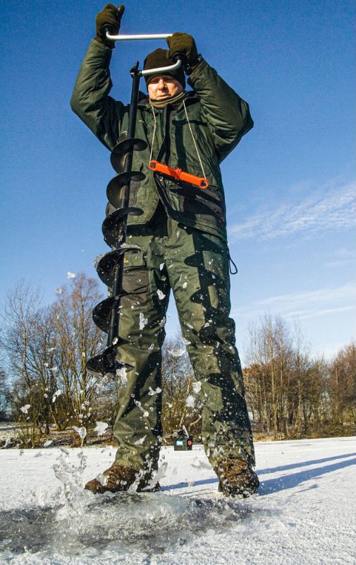 Angler mit Eisbohrer im Winter